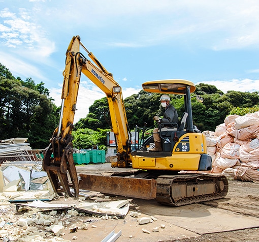 グラップル付きのミニ油圧ショベルで建設廃材を処理するヘルメット着用の作業員